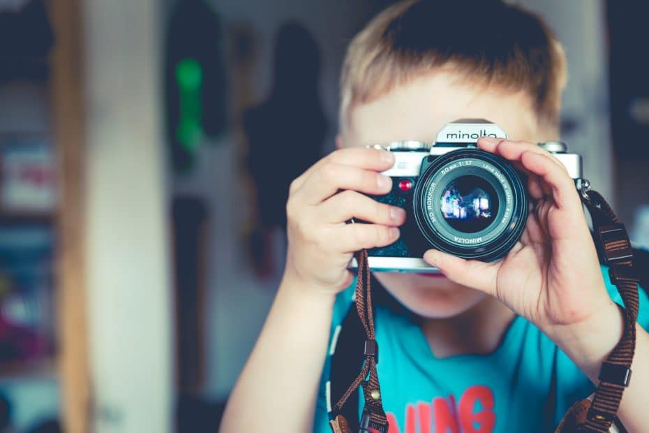 selective focus photography of boy holding gray Minolta bridge camera